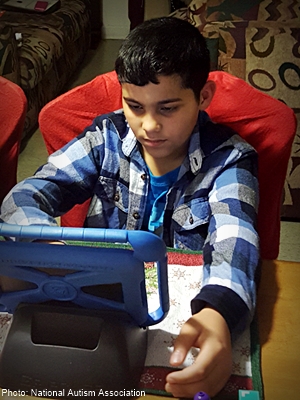 a dark-haired boy sitting at a table learning with his tablet