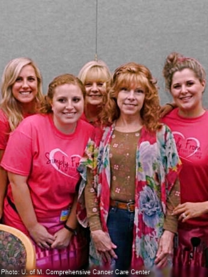 woman in strawberry blond curly wig surrounded by nurses in pink shirts